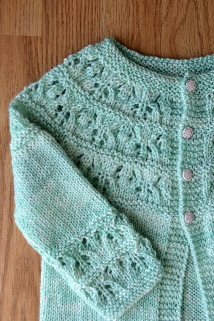 green baby cardigan with a lace stitch yoke and cuffs