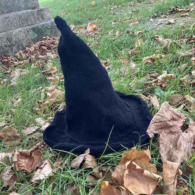 A classic, pointy black witch hat knit in aran weight yarn, featuring a smooth stockinette cone and a dramatically flared brim.