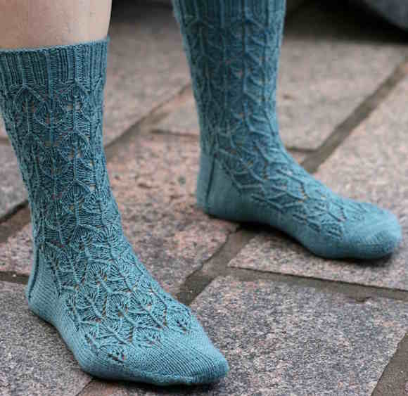 A top-down view of a knitted sock featuring a solid-colored interlocking leaf lace pattern that grows seamlessly from the toe, transitioning into a vertical rib at the cuff.