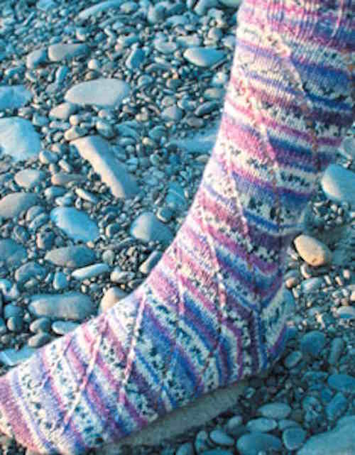 pair of knitted socks featuring opposing diagonal spiral patterns created by yarn overs and decreases, worked in a brightly variegated yarn to highlight the shifting columns.